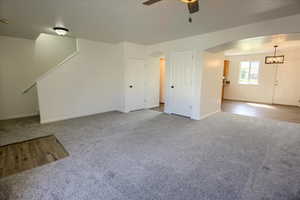Unfurnished living room featuring wood finished floors, ceiling fan with notable chandelier, arched walkways, carpet, and baseboards