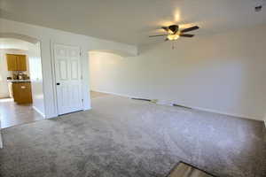 Carpeted spare room featuring arched walkways, baseboards, and ceiling fan