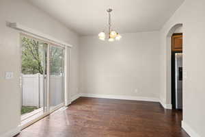 Unfurnished dining area with arched walkways, wood finished floors, baseboards, and an inviting chandelier