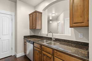 Kitchen featuring arched walkways, a sink, dark stone counters, dark wood finished floors, and dishwasher