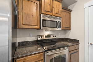 Kitchen with dark stone counters, brown cabinets, and appliances with stainless steel finishes