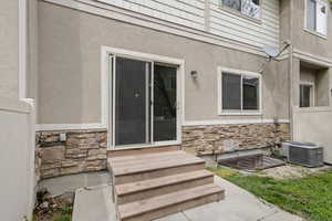 View of exterior entry featuring stone siding, fence, cooling unit, and stucco siding