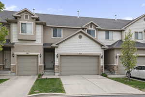 View of property with stone siding, an attached garage, a shingled roof, and concrete driveway