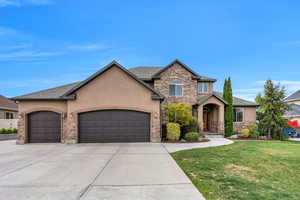 View of front of property with a front lawn, concrete driveway, an attached garage, stucco siding, and stone siding