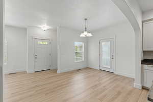 Foyer entrance featuring arched walkways, light wood-style floors, visible vents, and baseboards