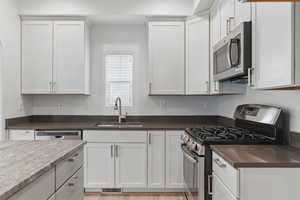 Kitchen with white cabinets, visible vents, stainless steel appliances, and a sink