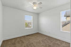 Carpeted spare room with a wealth of natural light, a ceiling fan, and baseboards