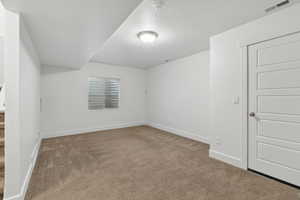 Spare room featuring carpet floors, a textured ceiling, visible vents, and baseboards