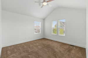 Empty room with carpet floors, visible vents, lofted ceiling, and a ceiling fan