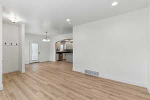 Unfurnished living room featuring light wood finished floors, baseboards, visible vents, and arched walkways