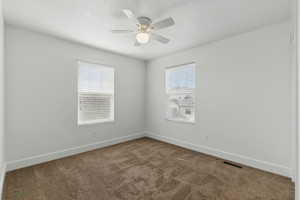 Empty room featuring carpet floors, visible vents, a ceiling fan, and baseboards