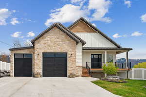 View of front of property featuring fence, concrete driveway, an attached garage, covered porch, and stone siding