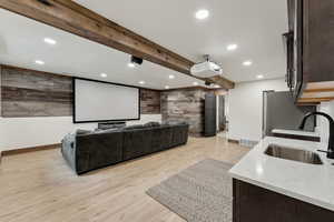 Cinema room with wood walls, visible vents, a sink, light wood-style floors, and baseboards