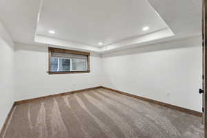 Empty room featuring carpet floors, a tray ceiling, and baseboards