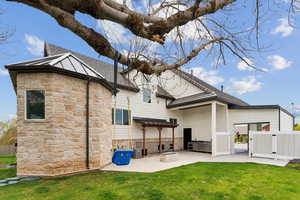 Rear view of property with a yard, a patio area, stone siding, and fence