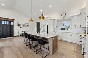 Kitchen with high quality appliances, a kitchen island with sink, light countertops, a kitchen bar, and backsplash