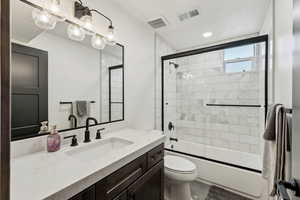 Bathroom featuring vanity, visible vents, bath / shower combo with glass door, and toilet
