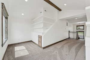 Unfurnished living room with beamed ceiling, carpet floors, visible vents, and baseboards