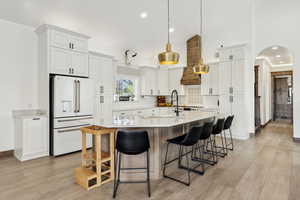 Kitchen featuring a large island, light countertops, arched walkways, decorative backsplash, and white fridge with ice dispenser