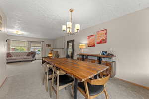 Dining area featuring carpet floors, a textured ceiling, baseboards, and an inviting chandelier