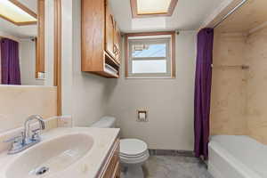 Full bath with toilet, vanity, shower / bath combination with curtain, baseboards, and stone finish floor