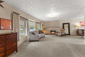 Living area with light carpet, a brick fireplace, baseboards, and a textured ceiling