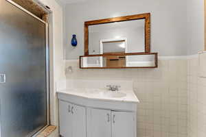 Bathroom featuring tile walls, vanity, a stall shower, and wainscoting