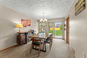 Dining area with a textured wall, baseboards, a chandelier, a textured ceiling, and light colored carpet