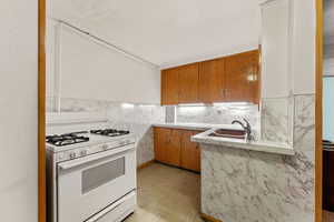 Kitchen featuring a sink, backsplash, white range with gas cooktop, brown cabinetry, and light countertops