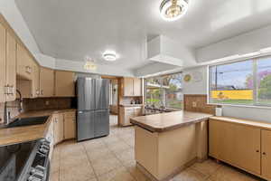 Kitchen featuring tile counters, stainless steel appliances, a sink, decorative backsplash, and a peninsula