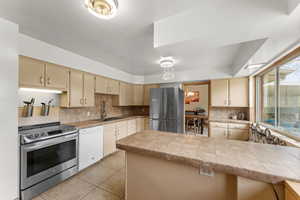 Kitchen with a sink, light tile patterned floors, cream cabinets, stainless steel appliances, and backsplash