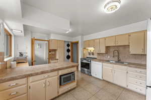 Kitchen with a sink, light tile patterned flooring, backsplash, cream cabinetry, and appliances with stainless steel finishes