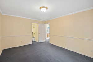 Unfurnished room featuring dark colored carpet, baseboards, and ornamental molding