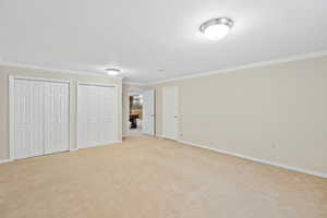 Unfurnished bedroom with light carpet, multiple closets, baseboards, and crown molding