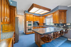 Kitchen featuring stainless steel appliances, carpet flooring, a sink, and brown cabinetry