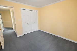 Unfurnished bedroom with dark carpet, baseboards, and ornamental molding