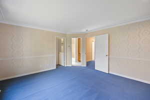 Unfurnished bedroom featuring wallpapered walls, dark carpet, and ornamental molding
