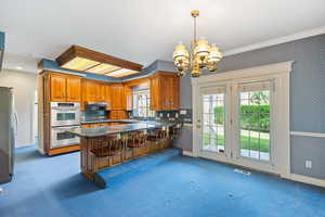 Kitchen with a peninsula, carpet floors, appliances with stainless steel finishes, and a notable chandelier