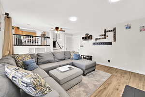 Living area featuring a ceiling fan, baseboards, light wood-style floors, and stairway