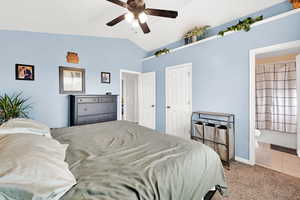 Tiled bedroom with ensuite bath, lofted ceiling, a ceiling fan, and carpet flooring