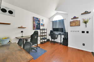Home office with lofted ceiling, wood finished floors, visible vents, and baseboards