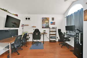 Office space with vaulted ceiling, wood finished floors, and baseboards