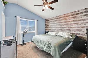 Bedroom featuring carpet flooring, vaulted ceiling, an accent wall, ceiling fan, and wooden walls