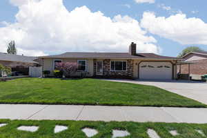 Ranch-style house with a chimney, concrete driveway, a front lawn with sprinkler, an attached garage, fence and carport for RV/Trailer storage