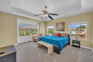 Carpeted bedroom featuring baseboards, a tray ceiling, and ceiling fan