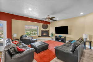 Living room featuring a ceiling fan, wood finished floors, a lit fireplace, baseboards, and recessed lighting