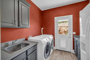 Laundry area featuring washing machine and clothes dryer, cabinet space, a sink, and light wood-style floors