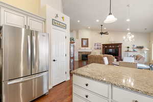 Kitchen with a stone fireplace, vaulted ceiling, freestanding refrigerator, dark wood-style flooring, and ceiling fan with notable chandelier