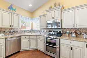 Kitchen with light stone counters, a sink, decorative backsplash, light wood-style floors, and stainless steel appliances