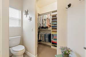 Bathroom with a walk in closet, toilet, and baseboards